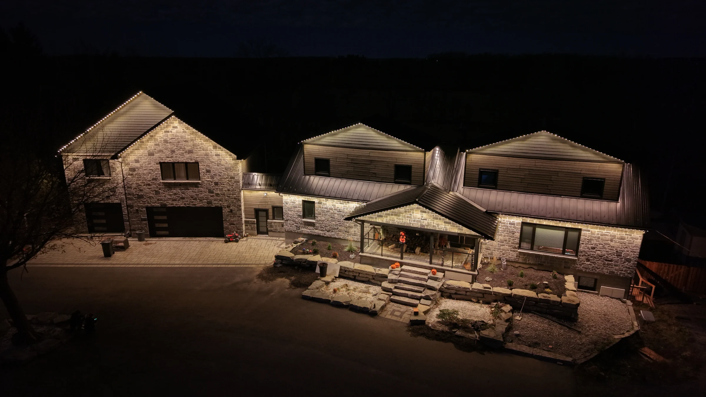 Night aerial view of a stone residence with warm roofline and exterior lighting.